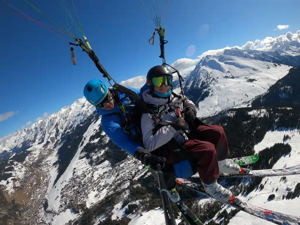 Vol acrobatique en parapente au-dessus de La Clusaz en hiver avec vue sur les sommets enneigés.